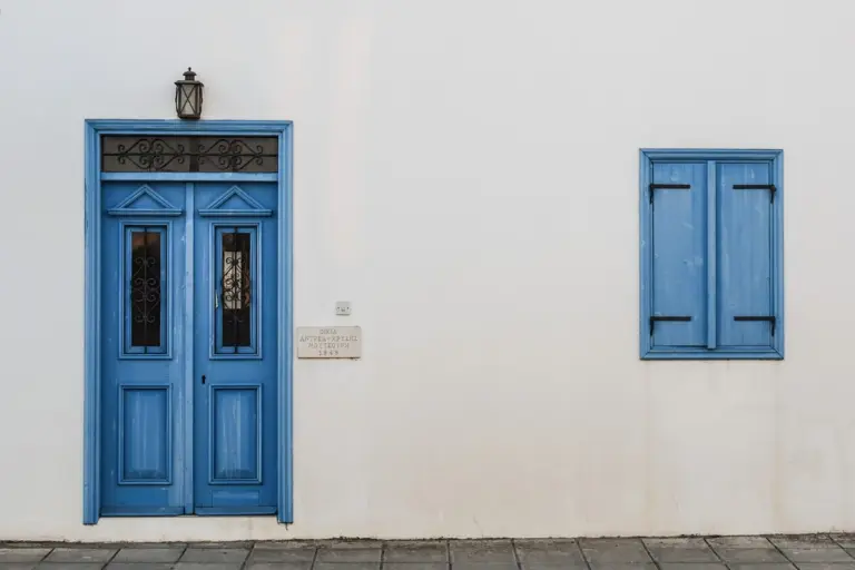 Blue front door and blue window shutters on a clean white exterior wall.