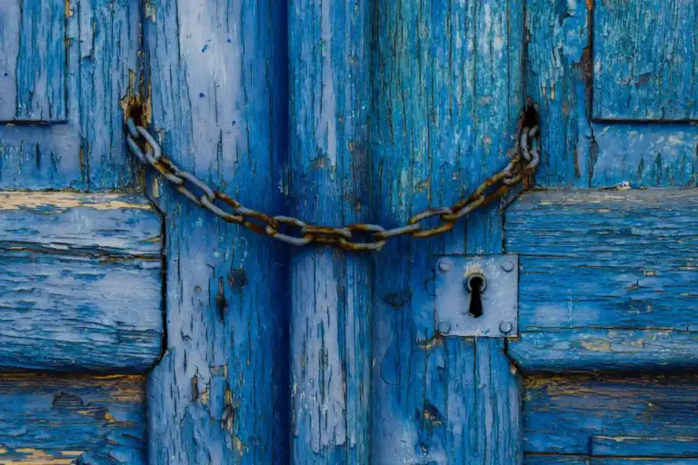 Blue weathered garage door with a metal chain draped across the center and a keyhole plate on the right side.
