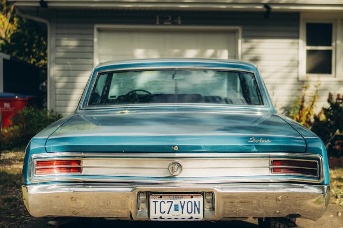 Rear view of a blue vintage car parked in a residential driveway with a closed garage door in the background.