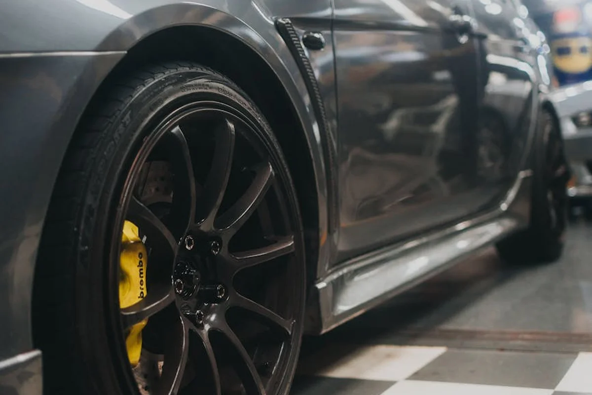 Close-up of a dark gray car wheel with a bright yellow brake caliper in a workshop setting