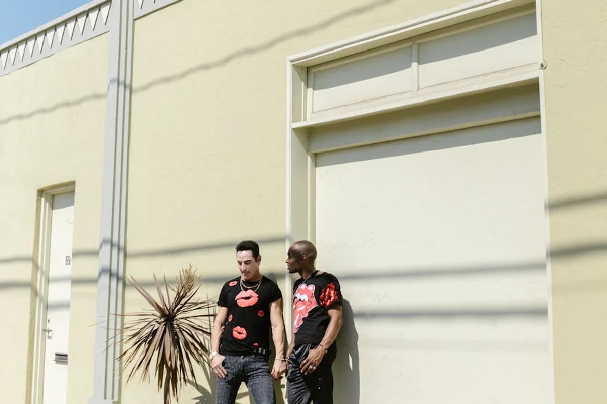 Two people stand outside a beige converted garage with a closed door and a potted plant nearby.