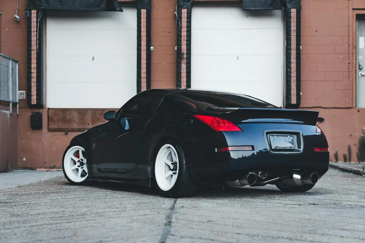 Black sports car with white rims parked in front of a row of beige garage doors.