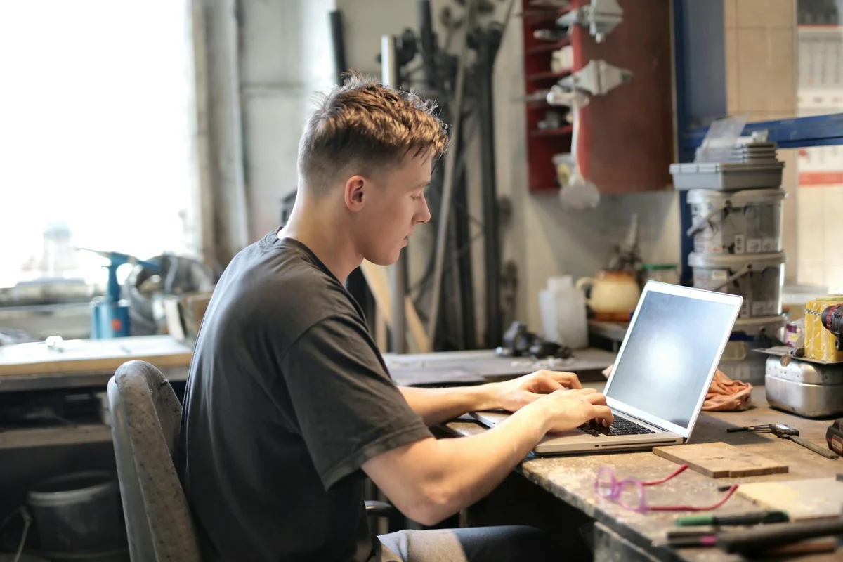 A person sits at a cluttered workshop bench using a laptop, likely programming a Craftsman garage door opener remote.