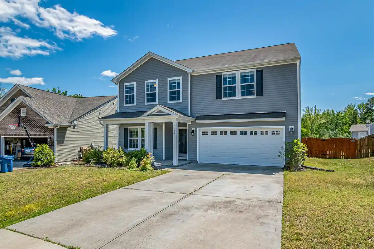 Two-story suburban house with a white two-car garage and a wide driveway under a clear blue sky.