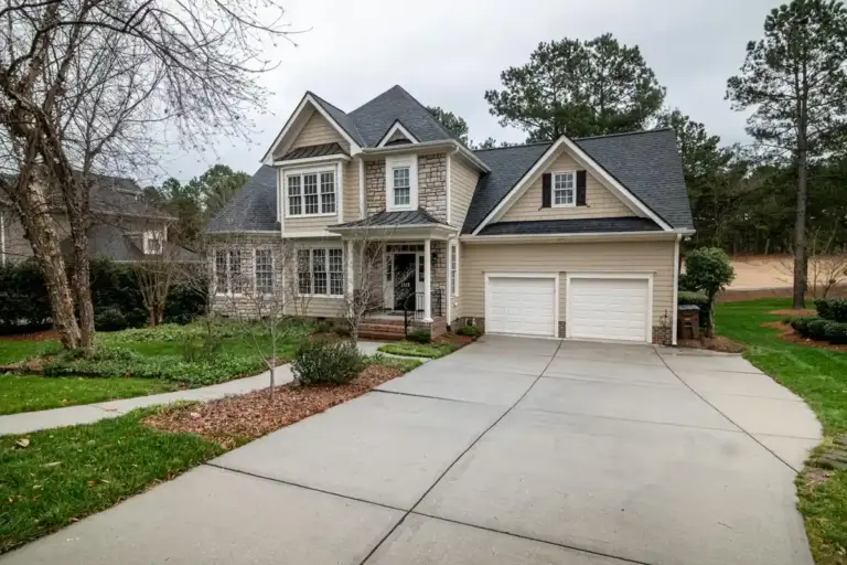 Front view of a two-story suburban house with a spacious concrete driveway leading to a two-car garage, with a manicured lawn and walkway.