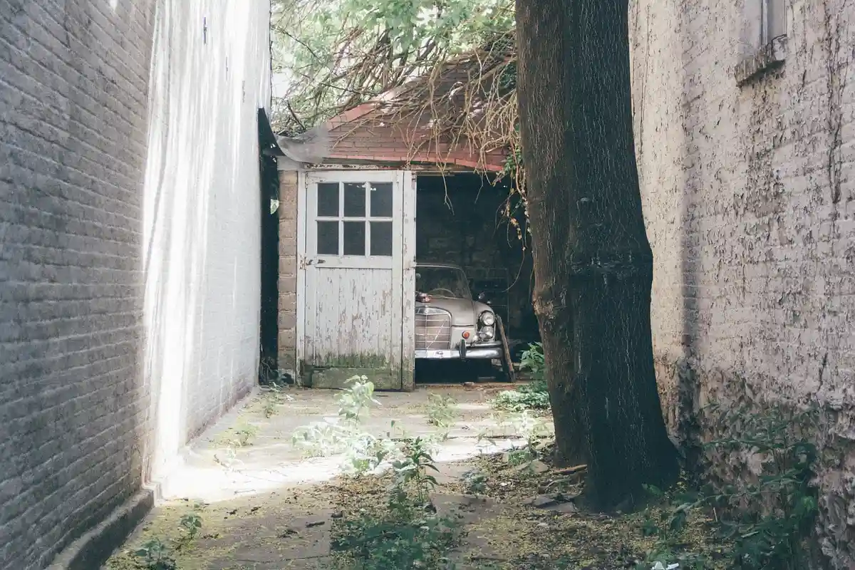 Narrow alley between brick buildings leads to a small detached garage with a car inside and the door partially open