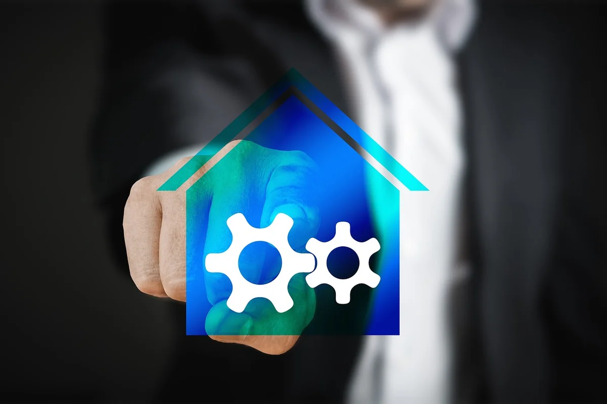 Hand pointing at two white gears inside a blue house icon, symbolizing maintenance of garage appliances.