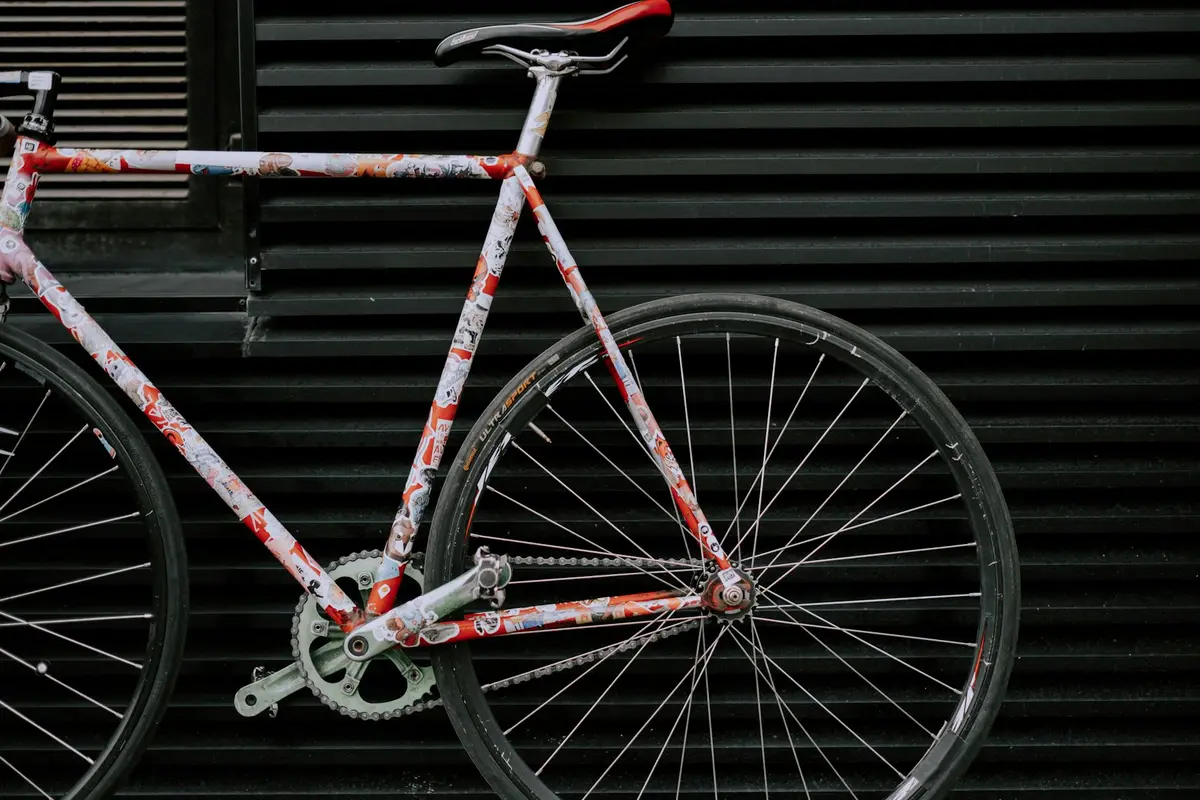 Vintage bicycle with a red and white patterned frame resting against a dark, horizontal garage wall.