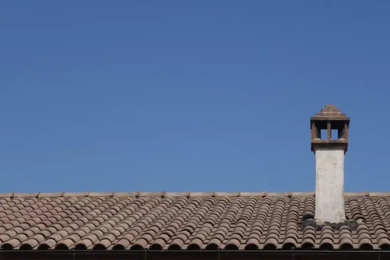 Clay tile garage roof with a chimney against a clear blue sky