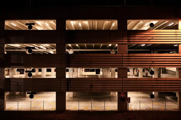 Interior of a dimly lit, multi-level parking garage with orange-toned lighting and repeating concrete levels