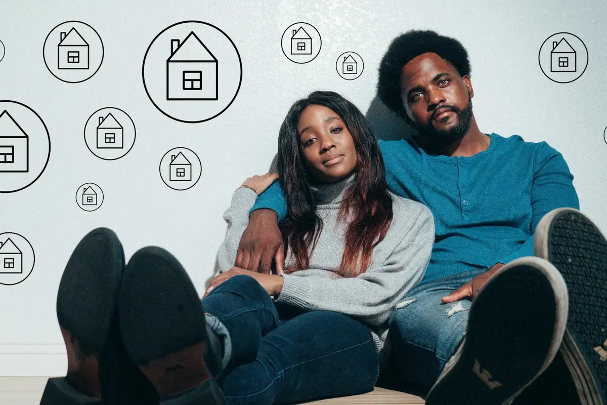 A couple sits on the floor against a wall decorated with circular house icons, symbolizing garage conversion ideas and permit considerations.