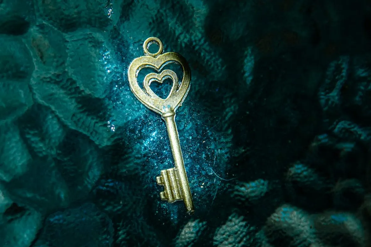 Close-up of a gold heart-shaped key resting on a dark teal, textured surface
