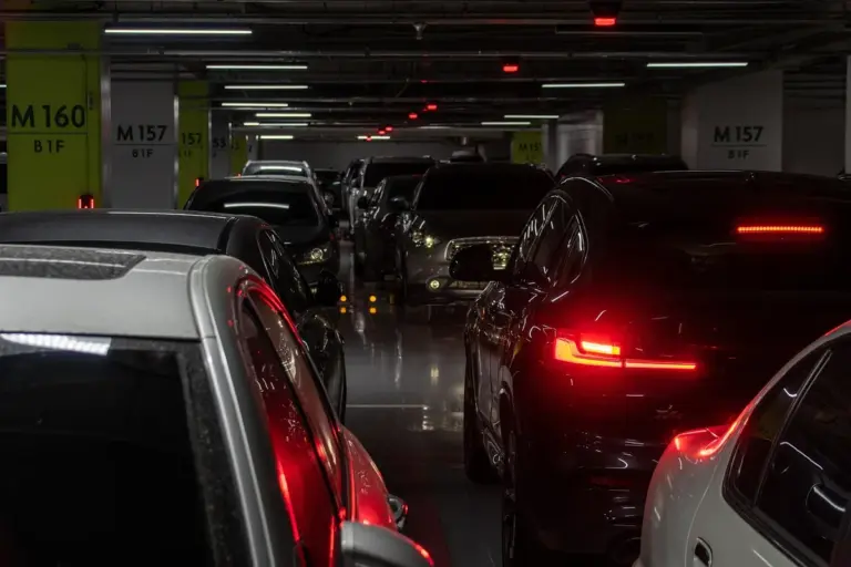 Underground parking garage filled with cars parked in rows under low ceiling and fluorescent lights.