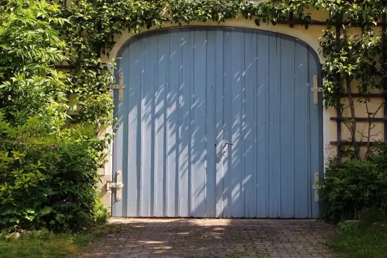 Blue arched garage door framed by greenery with sunlight filtering through leaves.