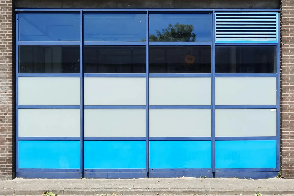 Blue sectional garage door with glass panels on the upper sections and solid blue panels on the lower sections.