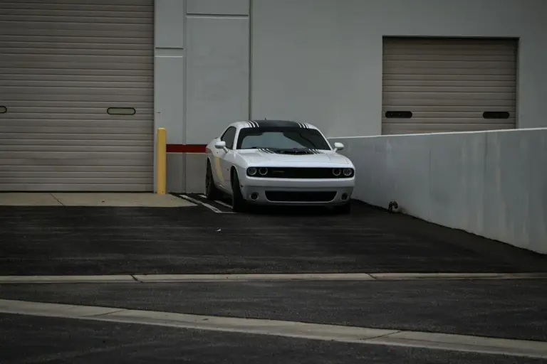 White car parked in front of a gray garage door with a concrete wall and asphalt pavement.