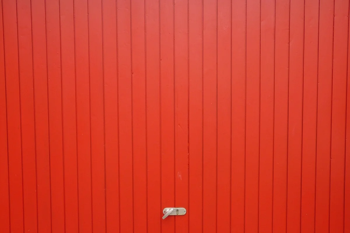 Close-up of a red garage door with a small metal latch near the bottom center.
