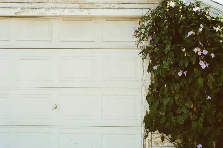 White paneled garage door with green ivy and small purple flowers along the right edge.