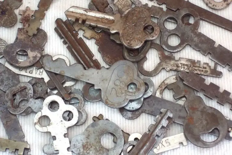 Close-up of a pile of assorted rusty keys and lock parts on a light surface.