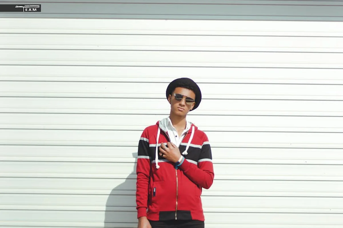 Person wearing a red and black jacket and a hat stands in front of a closed white garage door.