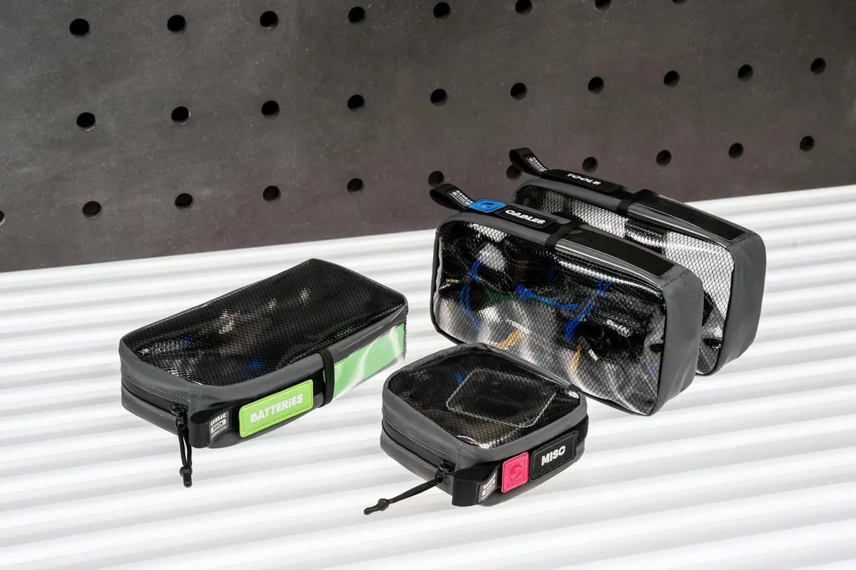 Three zipped battery organizers and pouches labeled BATTERY and MINI, arranged on a striped metal surface with a pegboard backdrop.