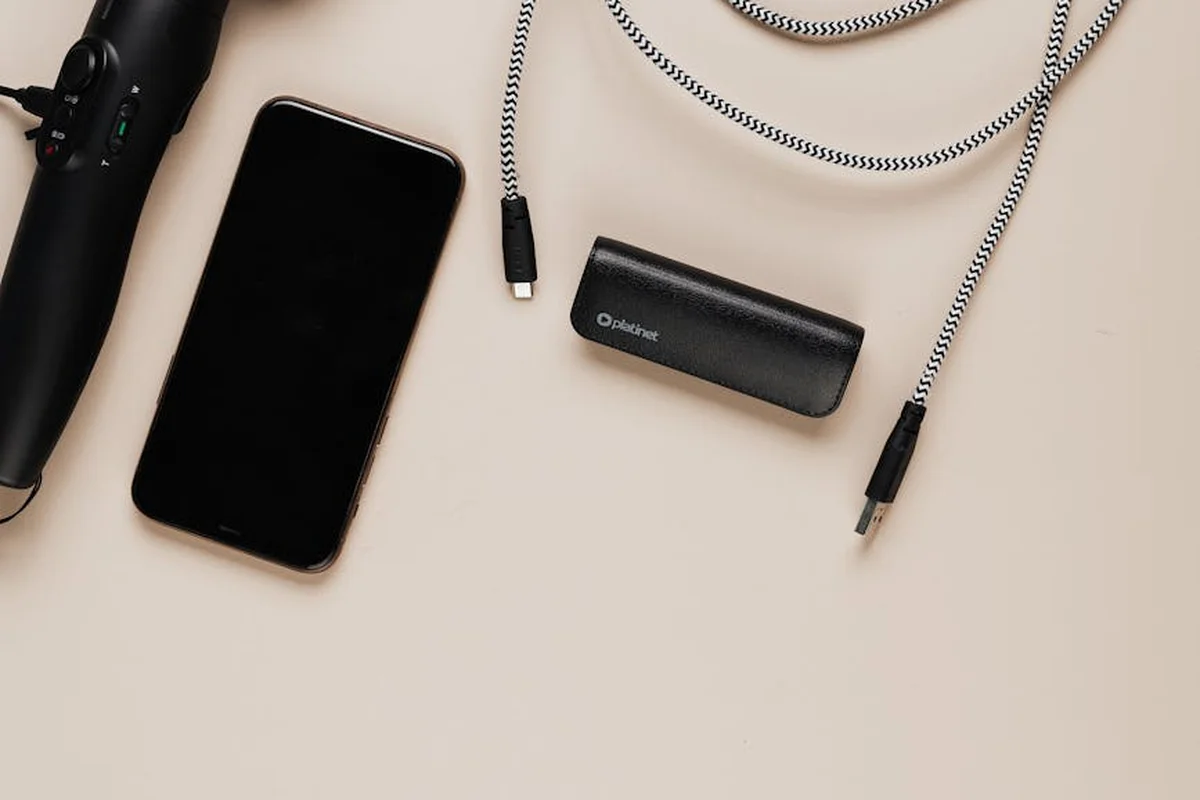 Flat lay of a smartphone, braided USB-C charging cable, and a small portable power bank on a light beige background.