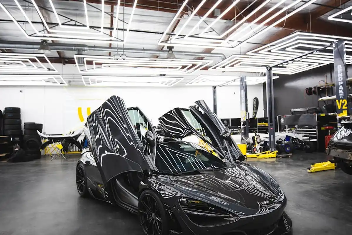 A sleek black sports car with its doors open in a bright, organized garage workshop.