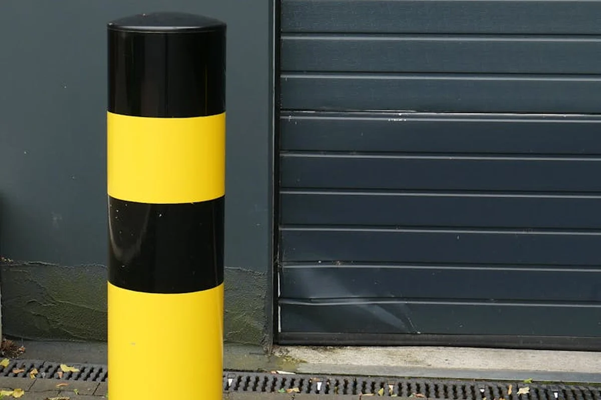Yellow and black striped bollard in front of a dark gray metal roll-up garage door.