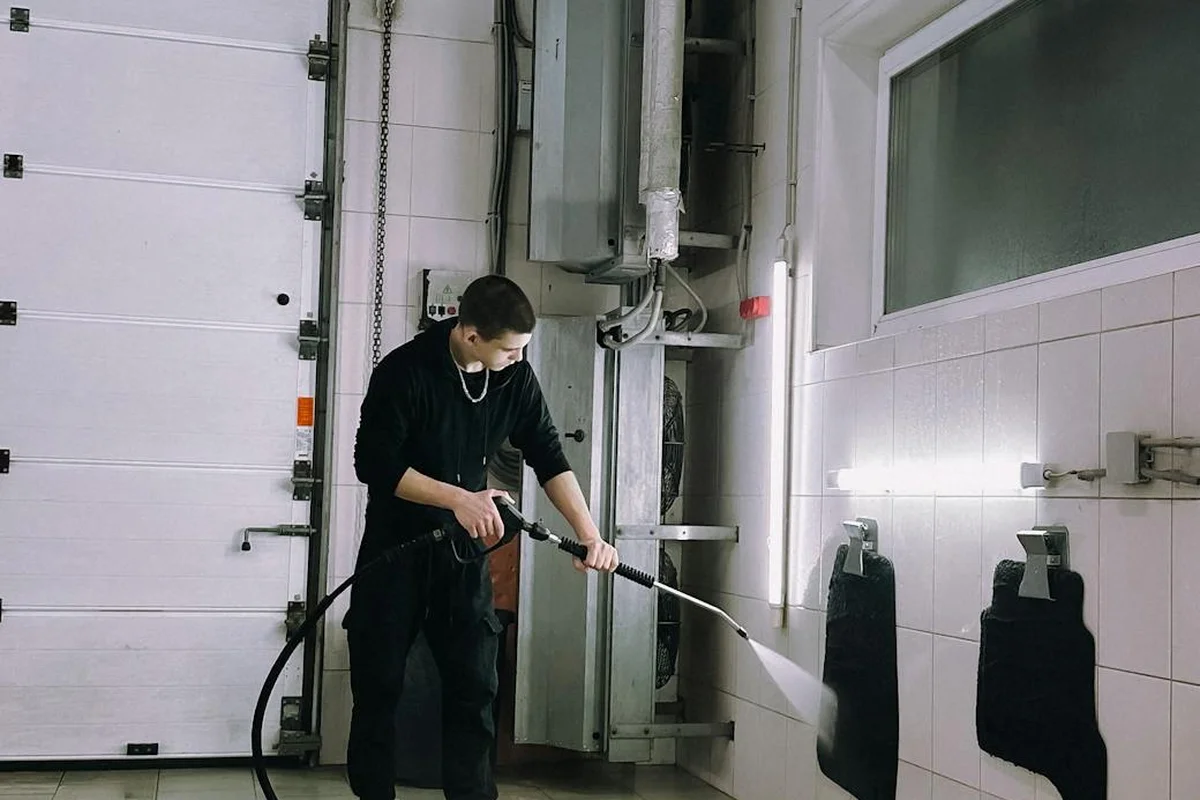 A person in dark clothing uses a spray gun connected to a hose in a garage, illustrating a tool from the gearhead’s checklist for painting a garage door.