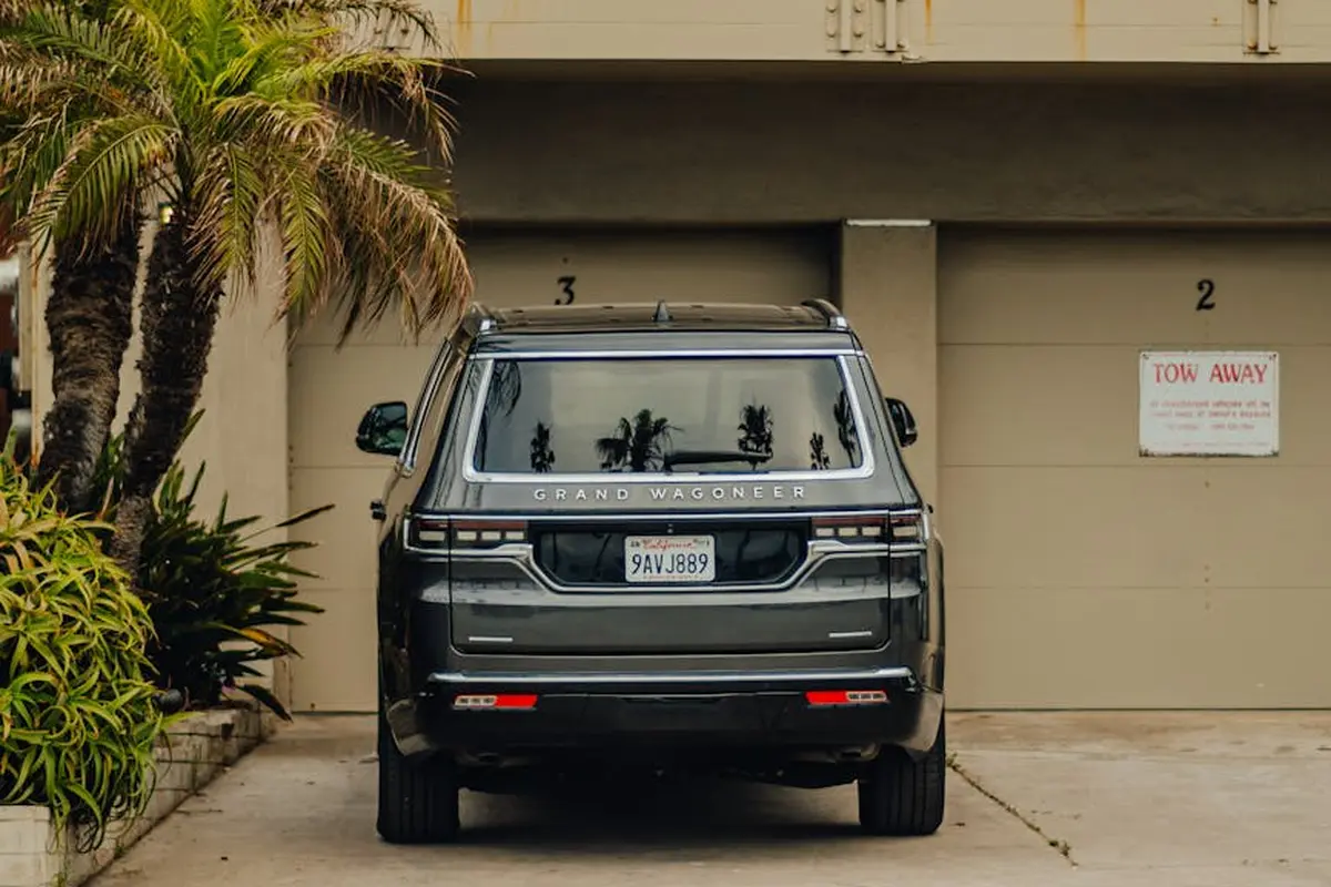 Rear view of a dark SUV parked in a driveway in front of a two-car garage, with palm trees on the left and a Tow Away sign on the right.