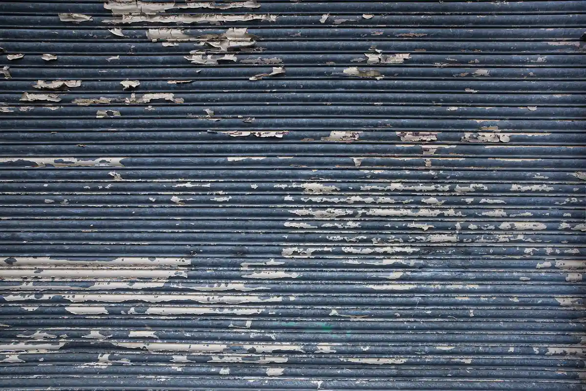 Blue-gray corrugated metal garage door with peeling paint and visible wear
