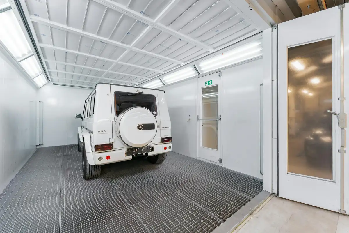 White SUV parked inside a bright, clean garage with a grated steel floor, white walls, and a glass exit door.