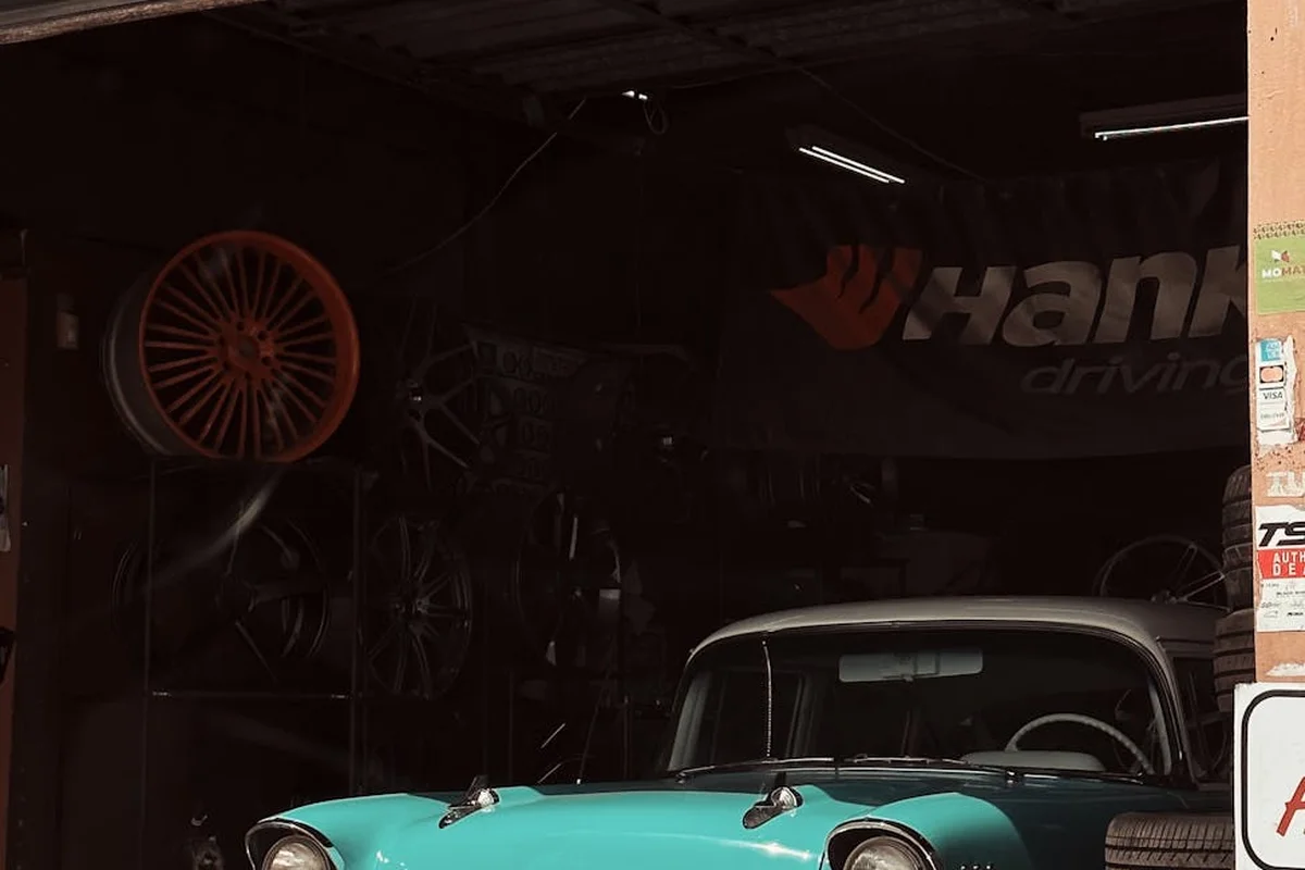 A vintage turquoise car in a dimly lit garage with rims on the wall.