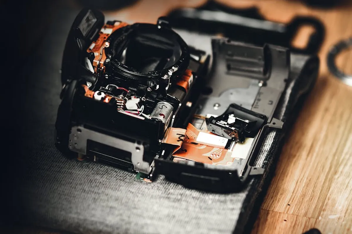Close-up of a disassembled garage door safety sensor unit with circuit boards exposed, laid on a wooden surface, preparing for bracket mounting.