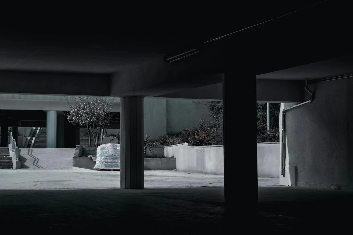 Dim parking garage with concrete pillars and shadows, illustrating the setting where garage door sensors may misalign or get dirty.