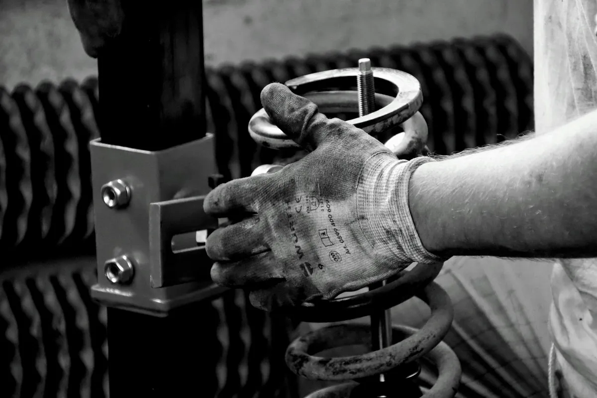 Close-up of gloved hands handling a garage door torsion spring and winding rod near the door mechanism.