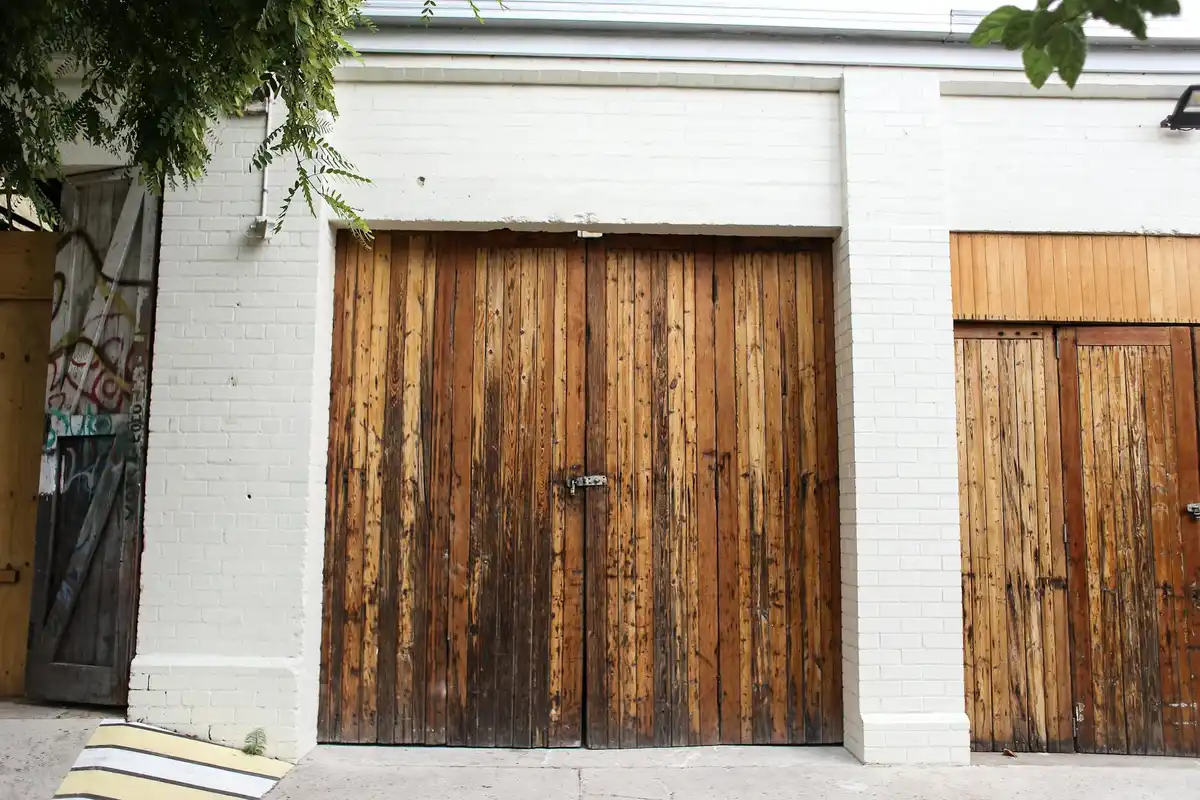Two tall wooden garage doors on a white brick building, with a central latch, no people in view.