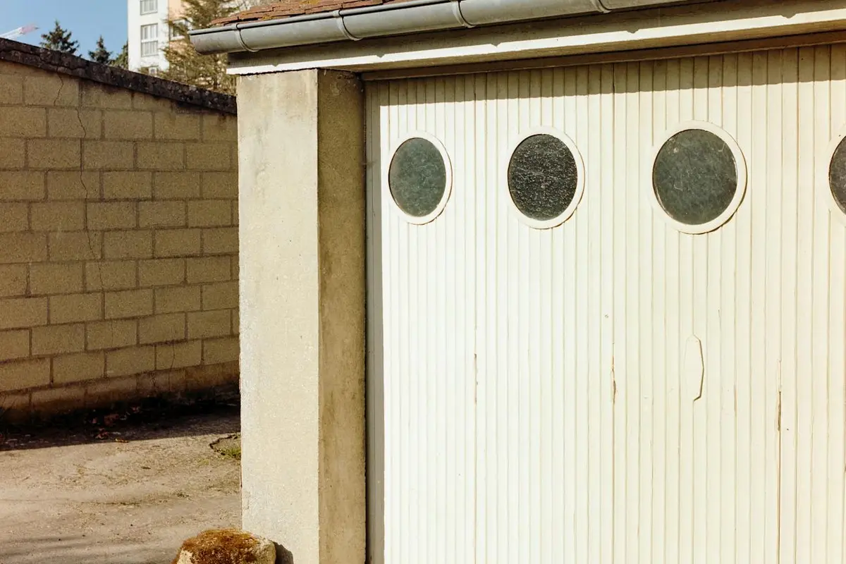 White garage door with circular windows showing gaps and alignment issues that require trimming for proper clearance.