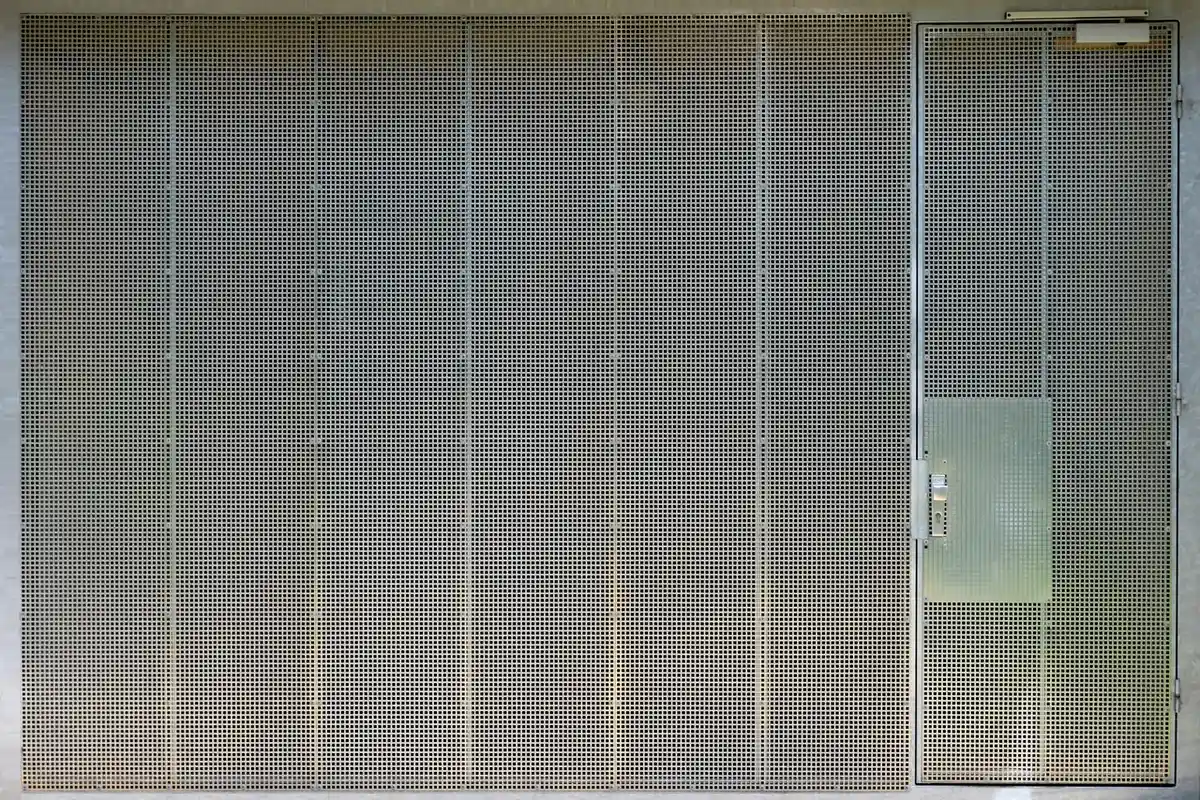 Exterior view of a large, vented metal sectional garage door with a small wall-mounted control panel on the right.