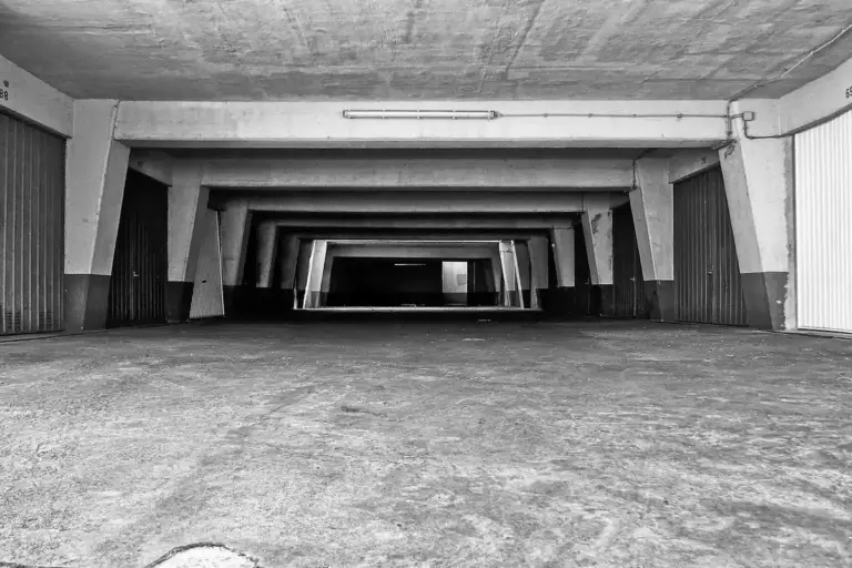 Black-and-white photograph of an empty underground parking garage with repeating concrete pillars receding into the distance.