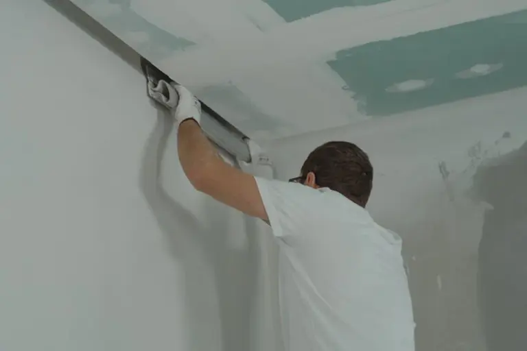 Tradesperson installing drywall on a garage ceiling, smoothing joint compound.