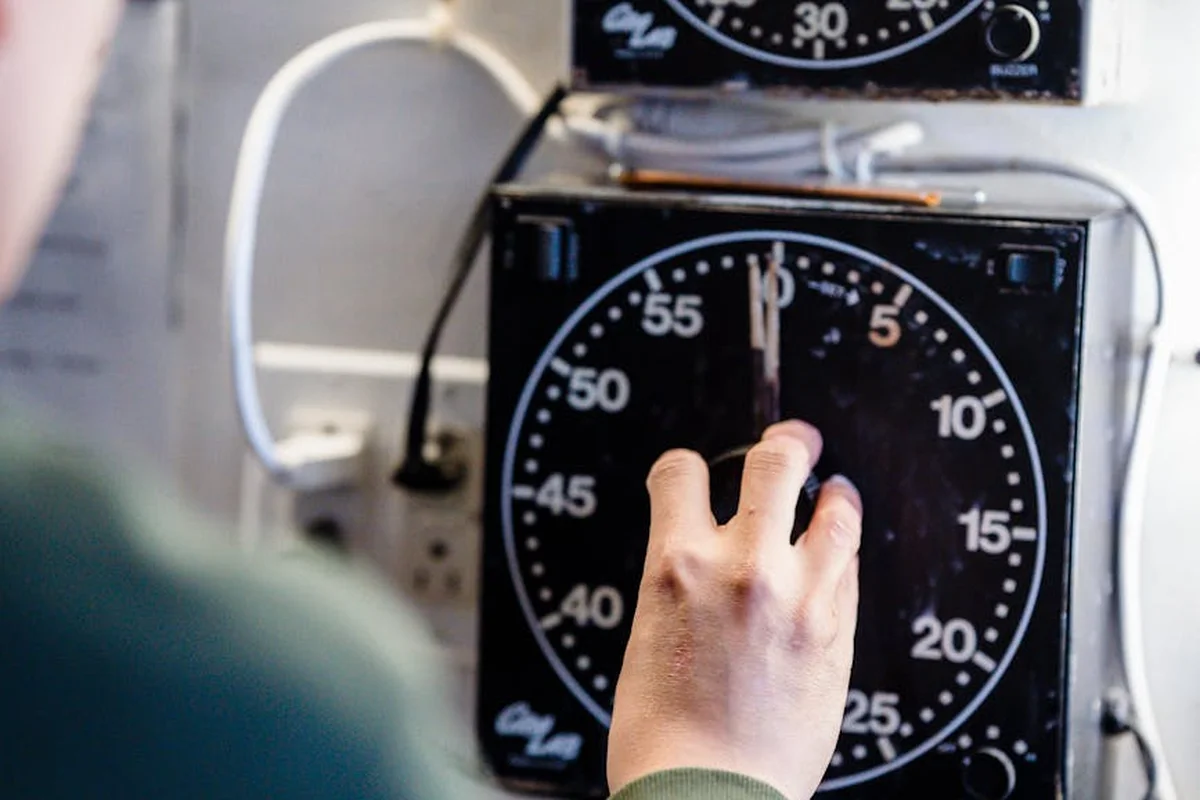 A hand turning a large analog timer dial on an electrical control panel in a garage.