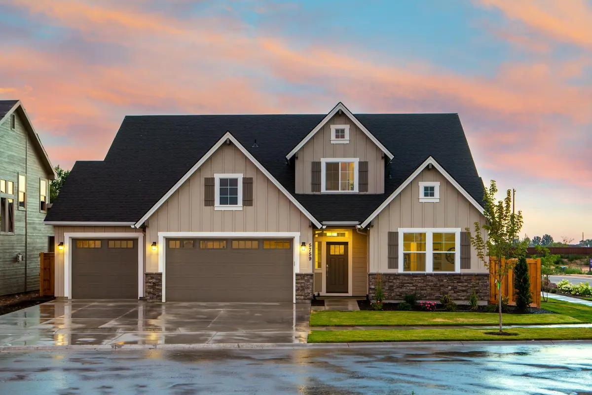 Exterior view of a two-car attached garage with beige siding, stone accents, and a manicured lawn at sunset.
