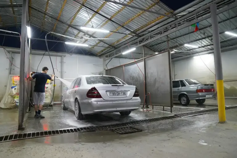A car being washed inside a professional garage bay with a wet concrete floor and a metal roof, illustrating a garage environment relevant to floor cleaning methods.