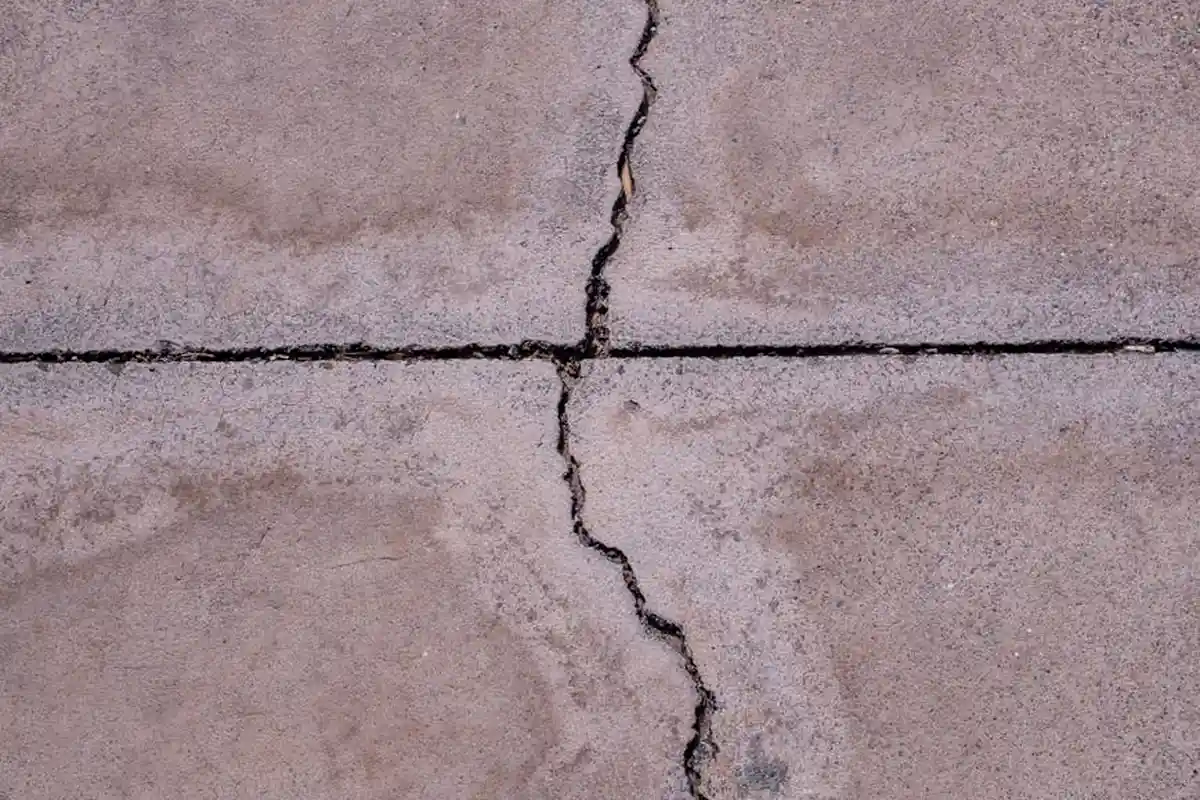 Close-up of a wide crack running through a concrete garage floor with a rough, stained surface.