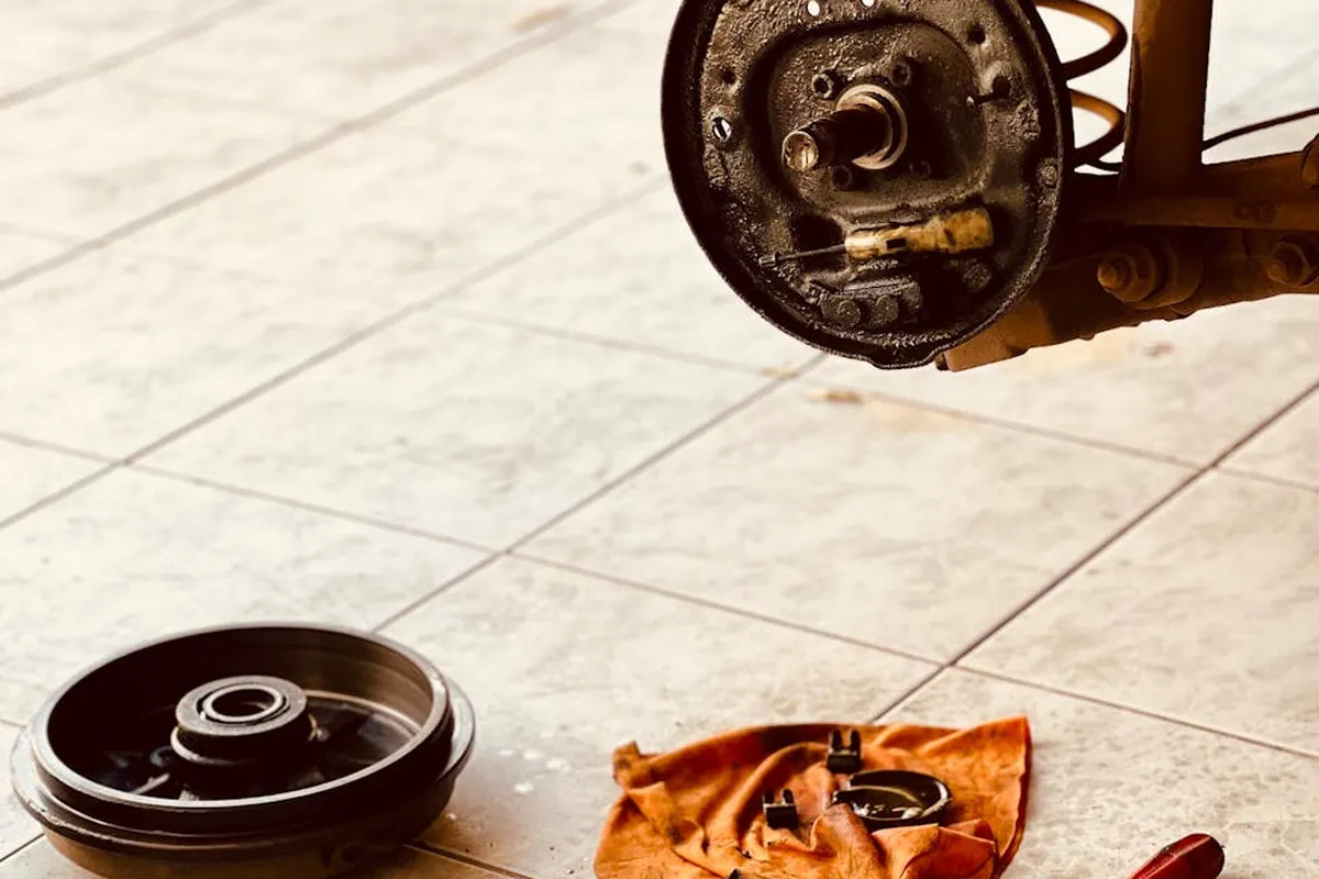 Garage floor prep scene featuring a removed wheel hub, an orange rag, and small tools laid out on beige tiles, illustrating the prep work for epoxy coating.