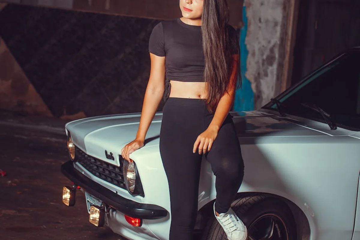 A person in black athletic wear leans against a light blue vintage car in a dimly lit garage, illustrating a garage workspace.