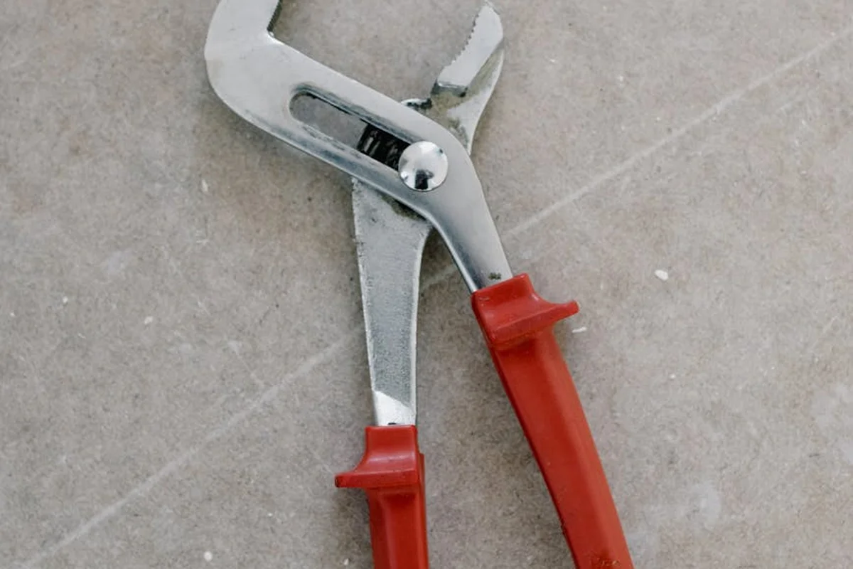 Close-up of a red-handled adjustable wrench resting on a concrete garage floor