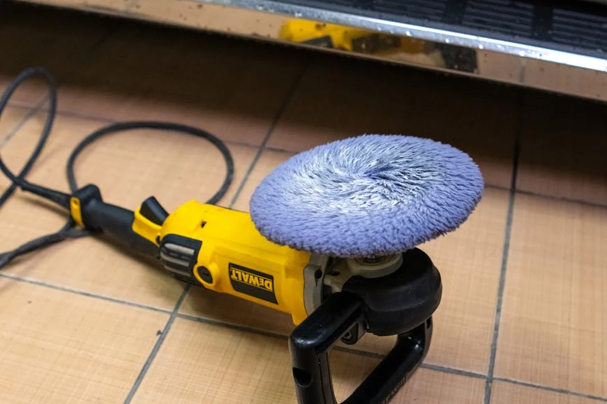 Yellow DeWalt power polisher with a blue pad resting on a tiled garage floor