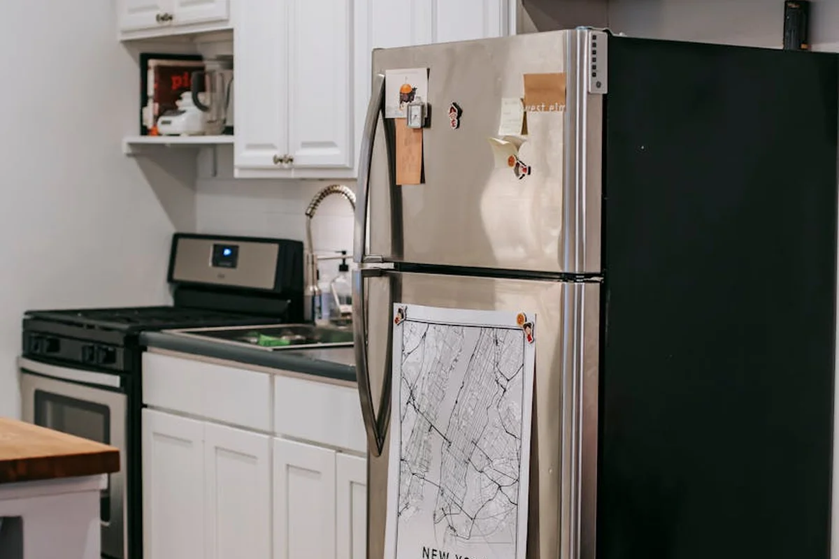 Stainless steel refrigerator in a white kitchen with magnets on the door and a map hanging from it